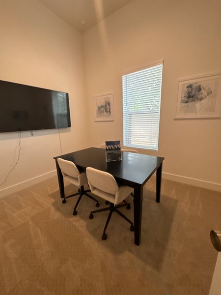 A cozy office with a sleek black table, white chairs, large TV, and framed art, perfect for productivity.