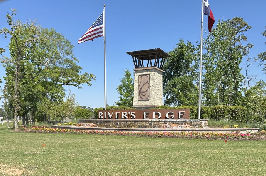 A welcoming entrance sign for River's Edge by Legend Homes, adorned with flags and surrounded by verdant greenery in Conroe, TX.