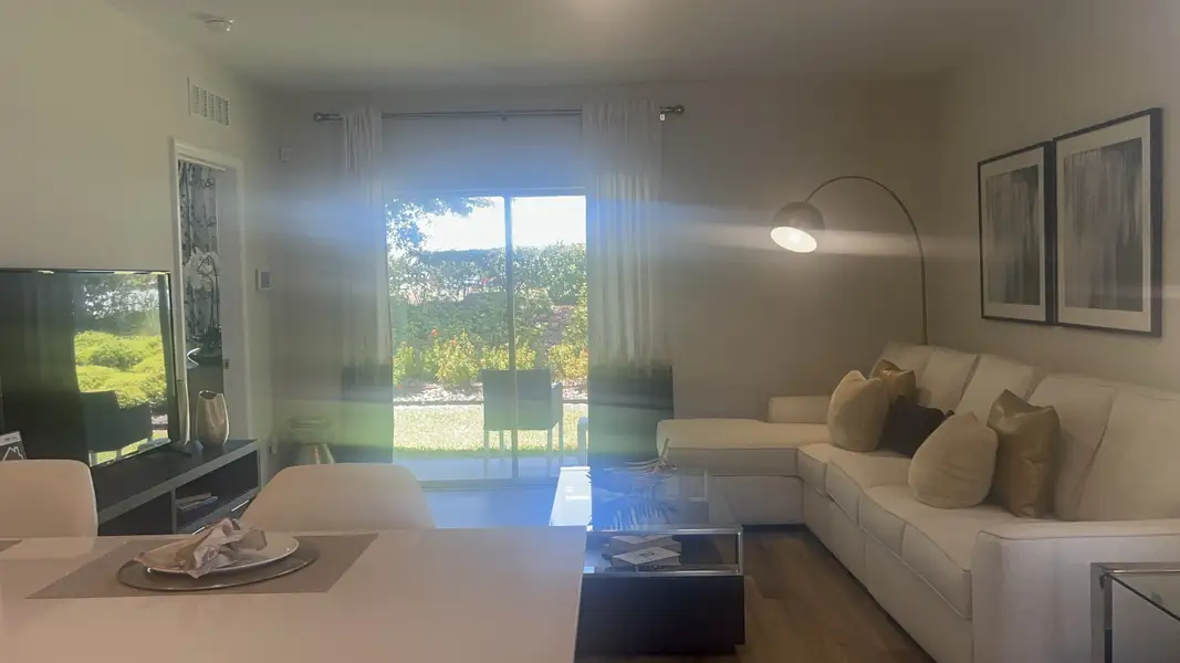 A cozy living room with a modern white sectional, glass table, and large window overlooking a lush garden.