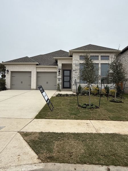 A modern brick home with a sleek entrance and manicured lawn at Parkside Peninsula 50' by Perry Homes (Georgetown, TX).