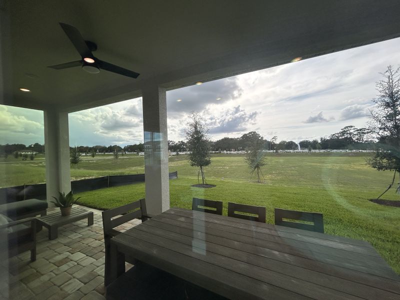 A cozy patio with a ceiling fan and outdoor seating offers serene views of a spacious green lawn and open sky.