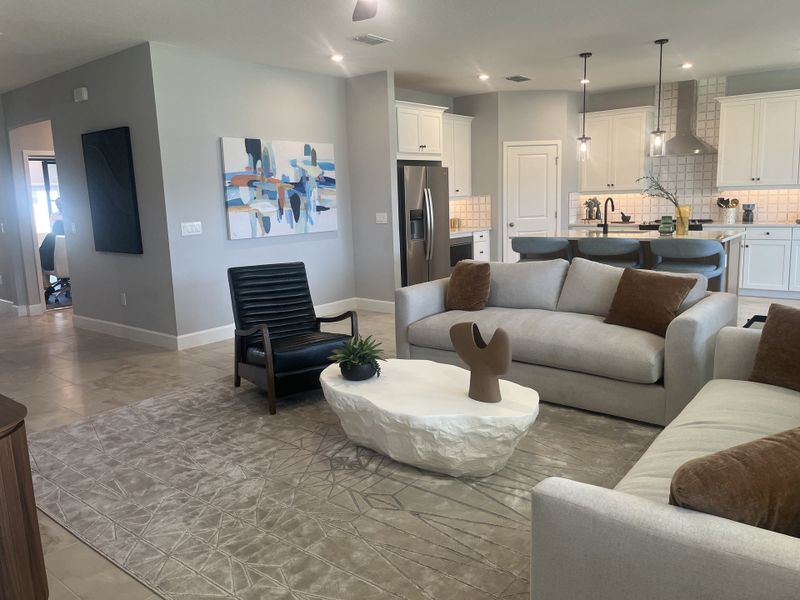 A modern living room with cozy sofas, abstract art, and an open kitchen with sleek white cabinetry.