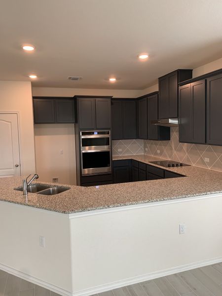 A modern kitchen with granite countertops, dark cabinetry, and stainless steel appliances, featuring recessed lighting.