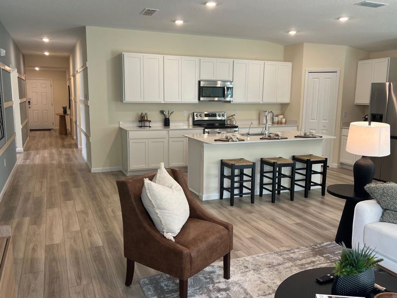 A modern open kitchen with sleek cabinets, cozy seating, and warm wood flooring, leading to a welcoming hallway.