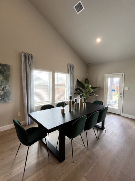 A modern dining area with a sleek black table, elegant green chairs, and natural light from large windows.