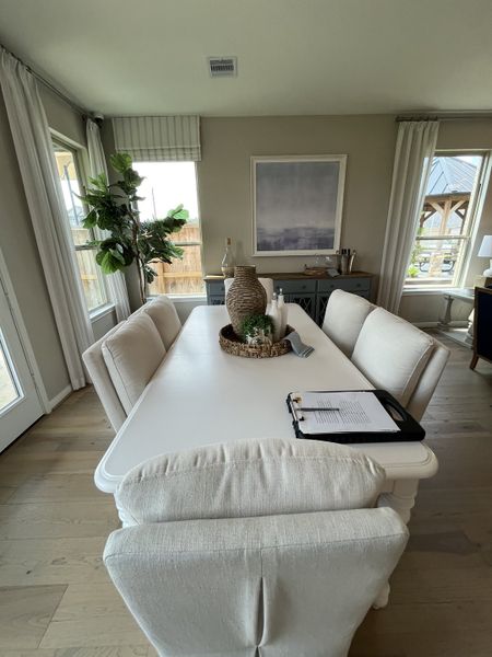 A cozy dining area with a white table, plush chairs, and natural light from large windows, complemented by minimalistic decor.