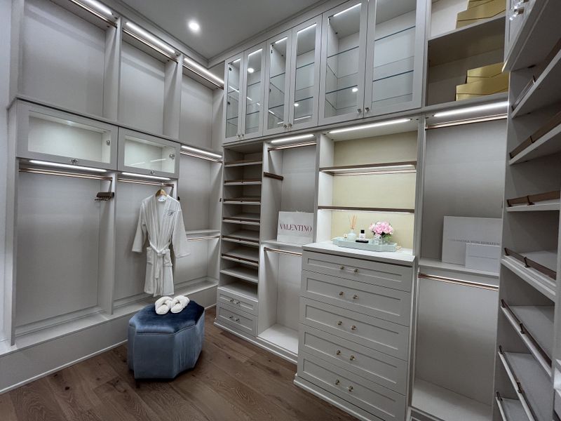 A luxurious walk-in closet with elegant cabinetry, spacious shelving, and warm lighting, complemented by a plush ottoman.