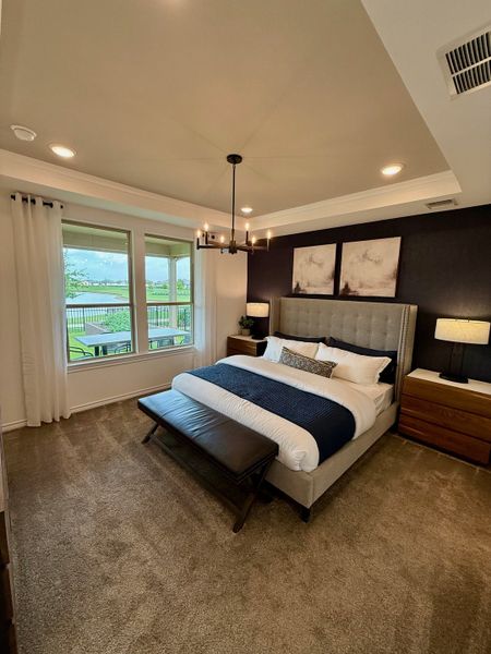 A cozy bedroom featuring a plush bed, modern chandelier, dark accent wall, and large windows with a serene view. A cozy bedroom featuring a plush bed, modern chandelier, dark accent wall, and large windows with a serene view.
