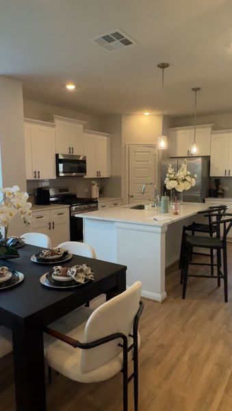 A modern kitchen with sleek white cabinets, an island, stainless steel appliances, and a cozy dining setup. A modern kitchen with sleek white cabinets, an island, stainless steel appliances, and a cozy dining setup.
