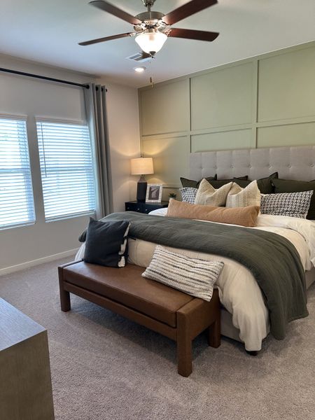 A cozy bedroom featuring a tufted headboard, neutral bedding, chic sconces, and a stylish ceiling fan.