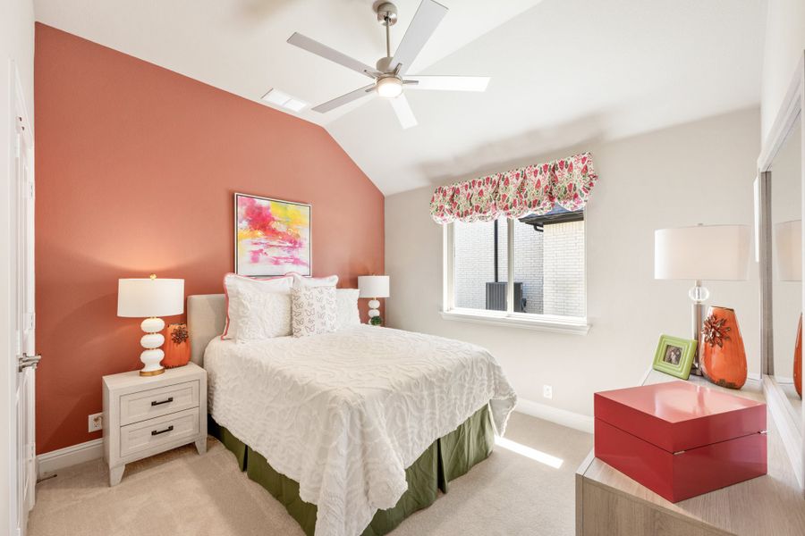 Bedroom with vaulted ceiling, ceiling fan, coral accent wall, and carpet flooring