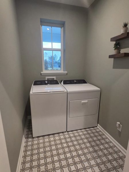 A compact laundry room with modern washer and dryer, stylish patterned tile flooring, and minimal wall decor.