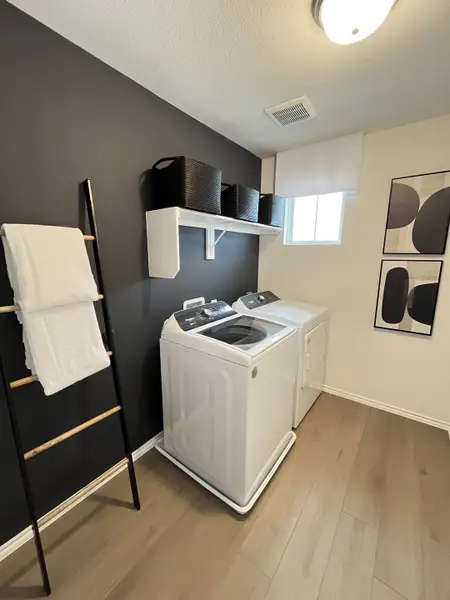 A modern laundry room with dark walls, sleek washer-dryer, ladder towel rack, and minimalist decor. A modern laundry room with dark walls, sleek washer-dryer, ladder towel rack, and minimalist decor.