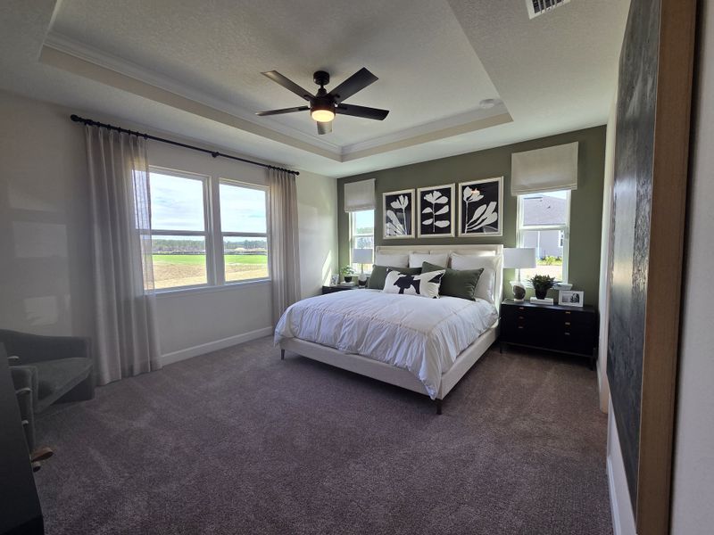 A serene bedroom with elegant decor, featuring a cozy bed, stylish artwork, and soft carpeting under a modern ceiling fan.
