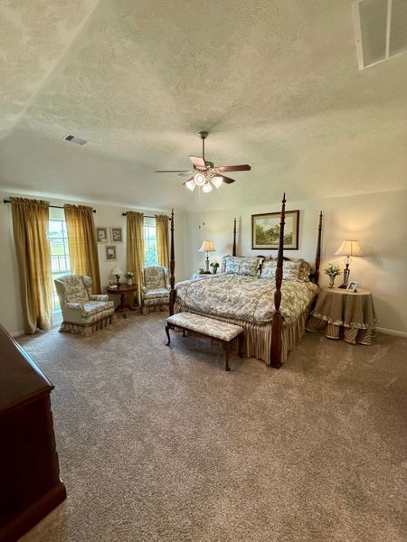 A spacious bedroom with elegant decor, featuring a cozy carpet, patterned bedding, and classic furniture.