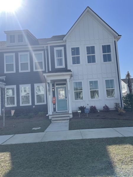 A modern townhome with contrasting dark and white siding, a bright teal door, and a paved walkway, located in Townhomes at Nexton by Brookfield Residential in Summerville, SC.