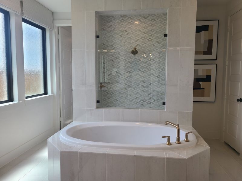 A spacious bathroom featuring a luxurious tub, geometric backsplash, and elegant gold fixtures.