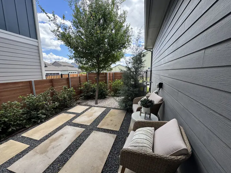 A cozy patio with wicker chairs, lush plants, and stepping stones, perfect for relaxation.