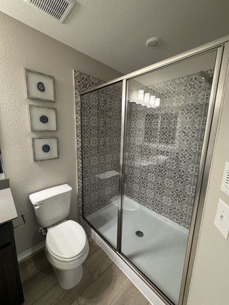 A modern bathroom featuring a patterned-tile shower, sleek glass doors, and elegant wall art. A modern bathroom featuring a patterned-tile shower, sleek glass doors, and elegant wall art.
