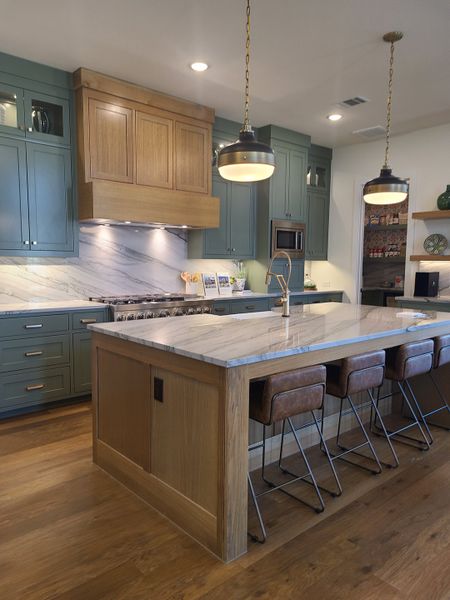 A modern kitchen featuring a large marble island, blue cabinetry, and stylish pendant lighting.