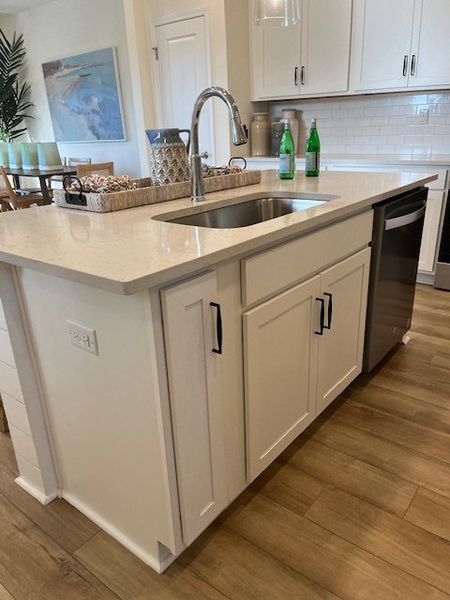 A modern kitchen with a sleek island, stainless steel sink, and elegant cabinetry, featuring chic flooring and a cozy atmosphere.