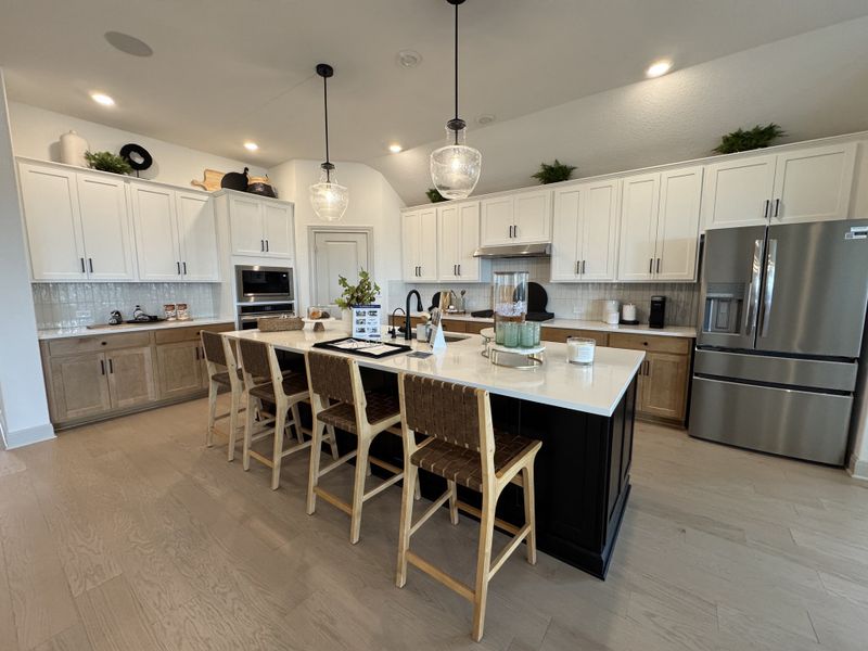A spacious kitchen featuring white cabinets, a central island with seating, stainless steel appliances, and elegant lighting.