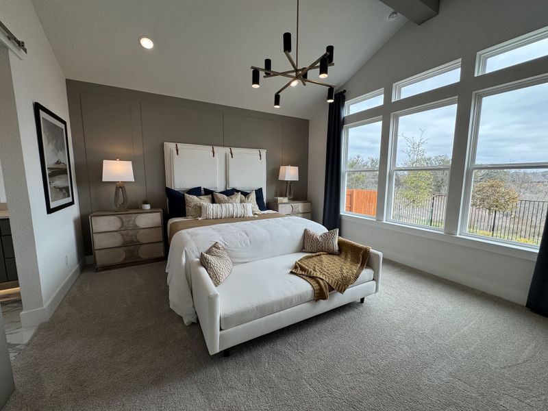 A cozy bedroom with large windows, a stylish chandelier, and a plush bed with elegant decor and neutral tones.