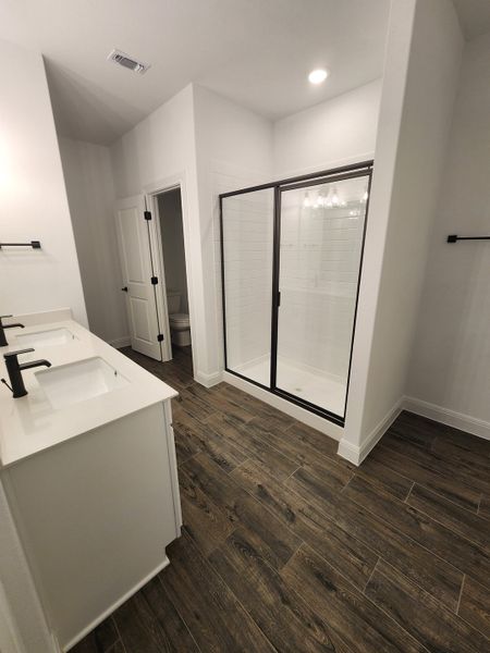 A modern bathroom featuring dual sinks, sleek fixtures, a glass shower, and wood-look flooring.