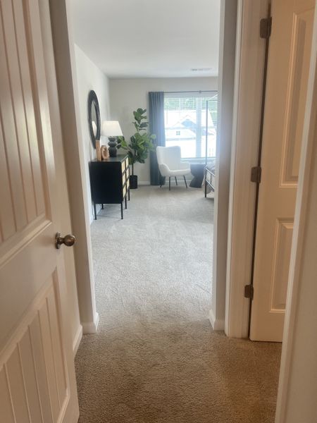 Cozy bedroom with soft carpeting, a plush chair by the window, and elegant decor in neutral tones.