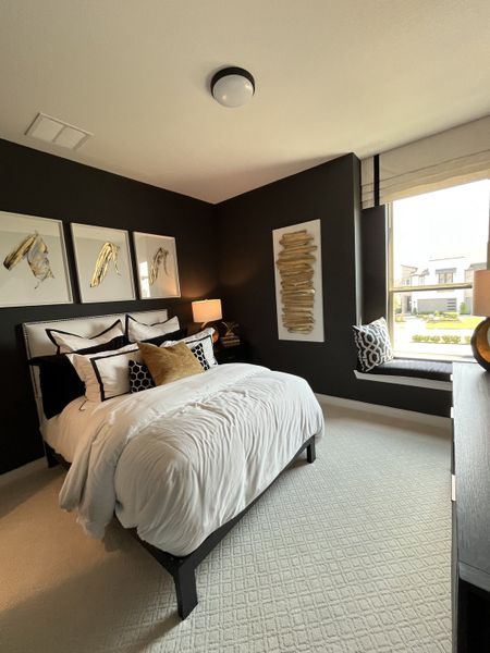 A cozy bedroom with dark accent walls, modern art, and a window seat for relaxation.