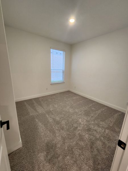 A cozy, carpeted room with a bright window, white walls, and recessed lighting. Ideal for a serene living space.
