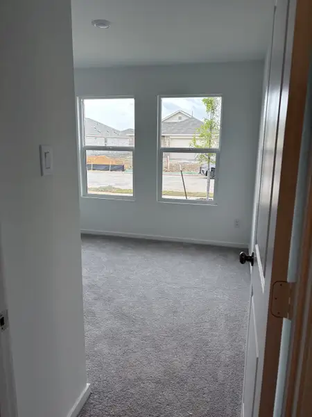 A bright, carpeted room with large windows offering ample natural light and a view outside.