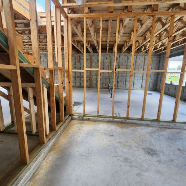 A home under construction featuring wooden framing and concrete floors, showcasing structural elements and space planning.