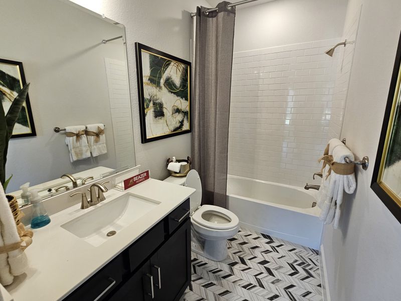 A chic bathroom featuring a stylish vanity, subway-tiled shower, and geometric-patterned floor with modern artwork.