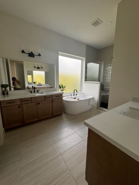 A spacious bathroom featuring a freestanding tub, dual sinks with wooden cabinetry, and a large mirror.