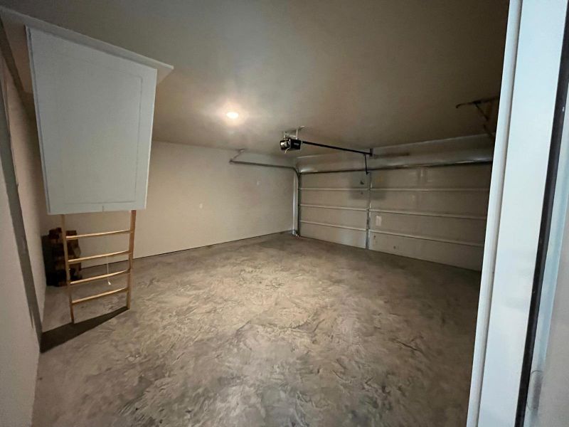 A spacious garage with a clean concrete floor, attic access, and ample space for two vehicles.