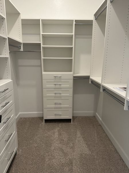 A spacious walk-in closet with sleek white shelving, ample drawers, and modern fixtures for organized living. A spacious walk-in closet with sleek white shelving, ample drawers, and modern fixtures for organized living.
