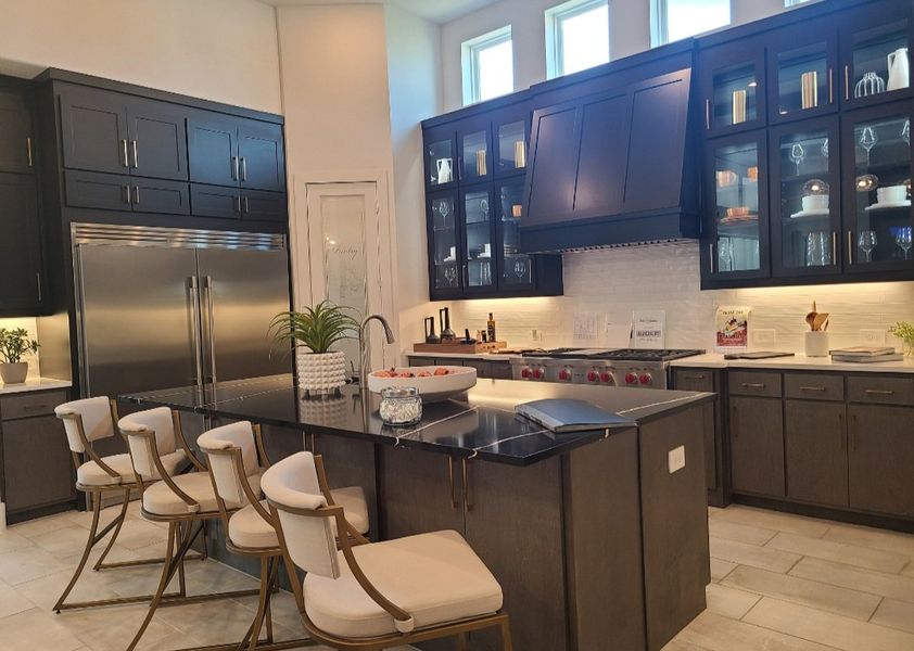 A modern kitchen featuring dark cabinets, stainless steel fridge, and an elegant island with stylish seating.