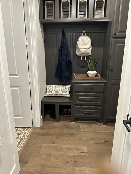 A functional mudroom with dark cabinetry, wood floors, and built-in storage including hooks and a bench.