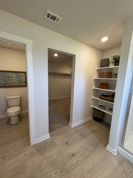 A spacious bathroom with light wood flooring, built-in shelves, and a walk-in closet adjacent to a toilet area.