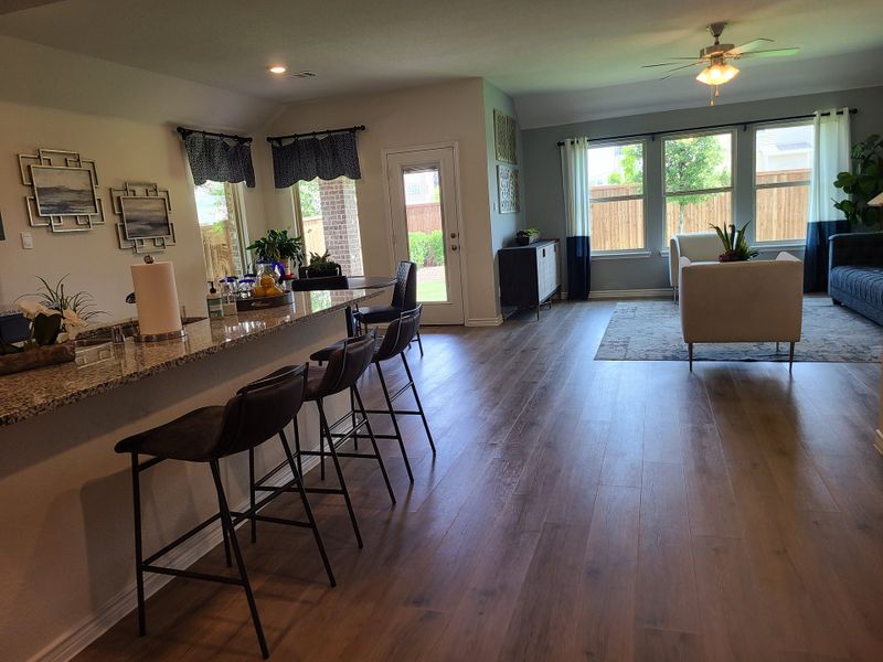 An inviting open-concept living area with a granite-topped breakfast bar, sleek seating, and large windows overlooking the backyard.