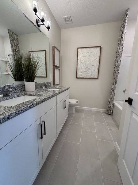 A modern bathroom featuring a dual-sink granite vanity, neutral tiles, and elegant artwork for a sophisticated touch.
