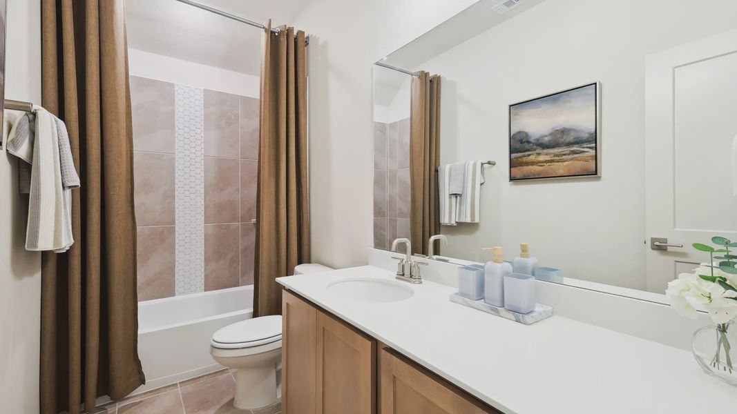 Elegant bathroom showcases a wood vanity and exquisite tile work in The Oaks community.