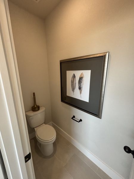 A compact half-bath with a toilet, simple decor, and a framed artwork of feathers, adding a natural touch. A compact half-bath with a toilet, simple decor, and a framed artwork of feathers, adding a natural touch.