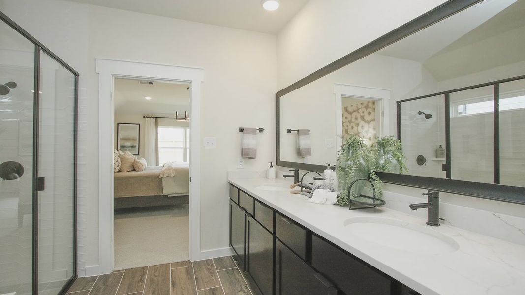 Luxurious dual vanity with marble countertop in Colony at Pinehurst. Elegant glass shower and wooden floors.