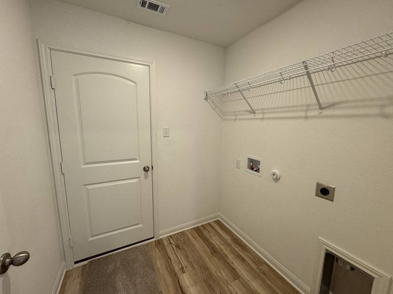 A utility room with a white door, wire shelf, and wood-look flooring.