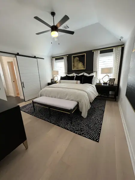 Sophisticated bedroom with a vaulted ceiling, black accent wall, modern fan, and sliding barn door.