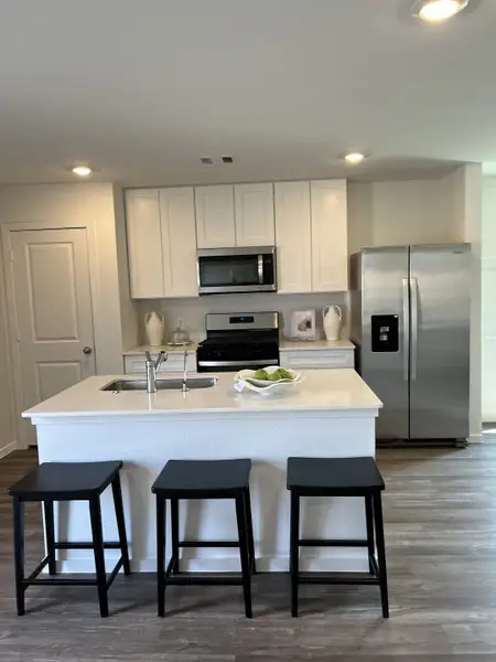 A modern kitchen with white cabinetry, an island with seating, stainless steel appliances, and sleek hardwood floors.