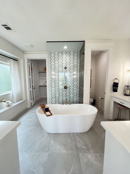 A modern bathroom with a freestanding tub, patterned shower wall, large window, and sleek finishes.