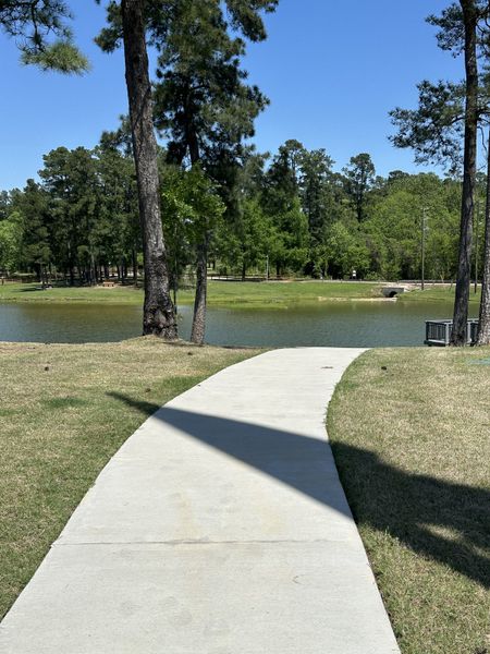 A scenic walkway by a tranquil pond amid lush greenery in Hills of Westlake by D.R. Horton (Conroe, TX).